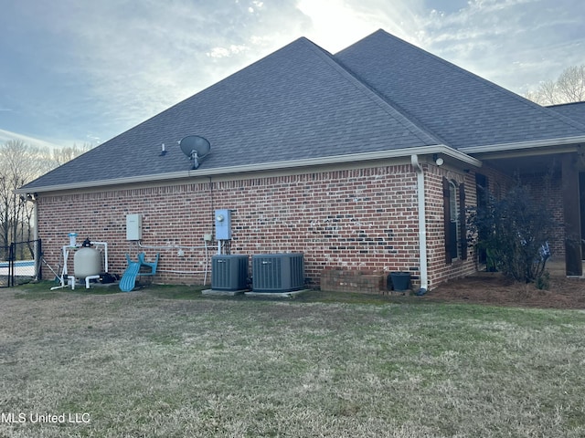 view of side of property featuring a yard, roof with shingles, central AC unit, and brick siding