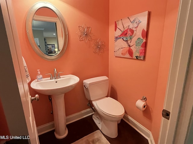 half bath featuring toilet, baseboards, and a sink