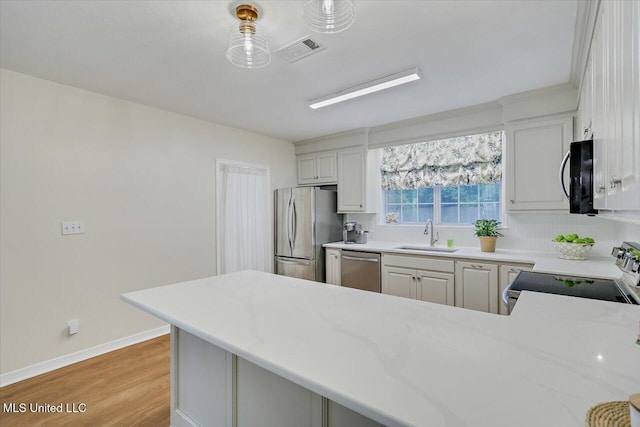 322 NW 2nd Ave, Magee, MS 39111 - kitchen featuring stainless steel appliances, light wood-style flooring, a peninsula, light stone counters, and white cabinetry