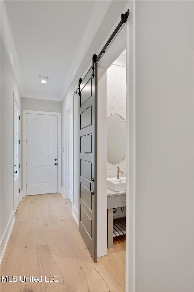 hallway with sink, a barn door, and light hardwood / wood-style flooring