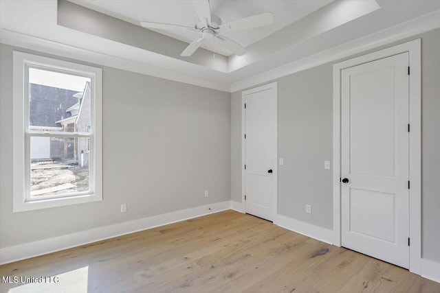 unfurnished bedroom with a tray ceiling, light wood-type flooring, and ceiling fan