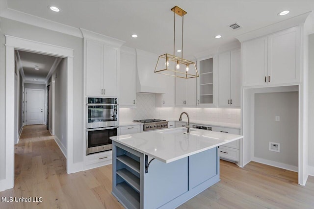 kitchen featuring a kitchen island with sink, light hardwood / wood-style flooring, decorative light fixtures, and white cabinets