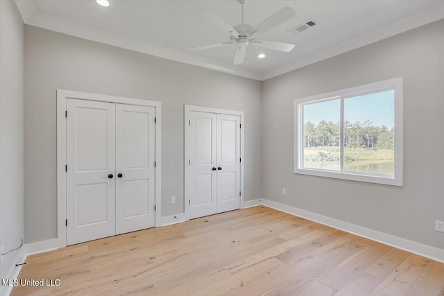 unfurnished bedroom featuring ornamental molding, two closets, light wood-type flooring, and ceiling fan