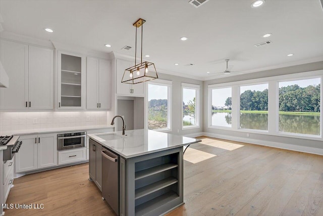 kitchen with a center island with sink, white cabinetry, light wood-type flooring, decorative light fixtures, and sink