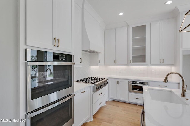 kitchen featuring custom exhaust hood, white cabinetry, stainless steel appliances, light hardwood / wood-style floors, and sink