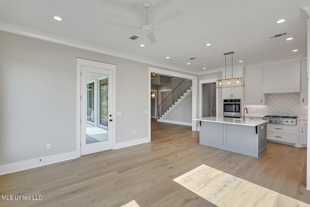 kitchen featuring a kitchen island with sink, white cabinets, decorative light fixtures, light wood-type flooring, and appliances with stainless steel finishes