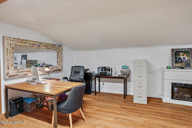 office area with light hardwood / wood-style floors, a textured ceiling, and vaulted ceiling