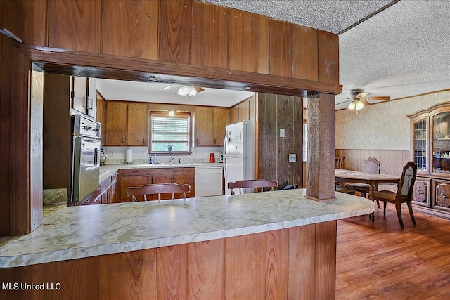 kitchen featuring white appliances, kitchen peninsula, a textured ceiling, and light wood-type flooring