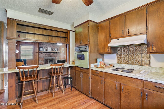 kitchen with oven, kitchen peninsula, a kitchen bar, light hardwood / wood-style flooring, and white electric stovetop