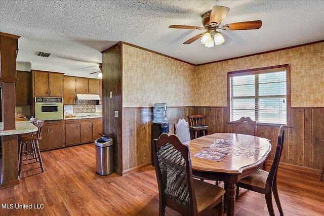 dining area featuring a textured ceiling, wooden walls, light wood-type flooring, and ceiling fan