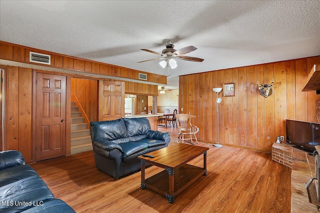 living room with light hardwood / wood-style floors, wood walls, a textured ceiling, and ceiling fan