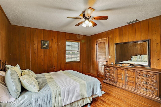 bedroom with ceiling fan, wood walls, a textured ceiling, and light hardwood / wood-style flooring