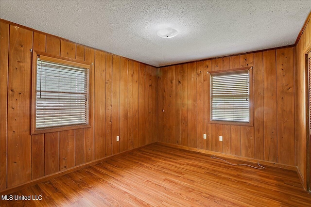 unfurnished room featuring plenty of natural light, wood walls, a textured ceiling, and light wood-type flooring