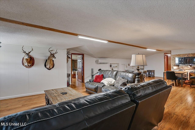 living room featuring light hardwood / wood-style floors, a textured ceiling, lofted ceiling, and a wall unit AC