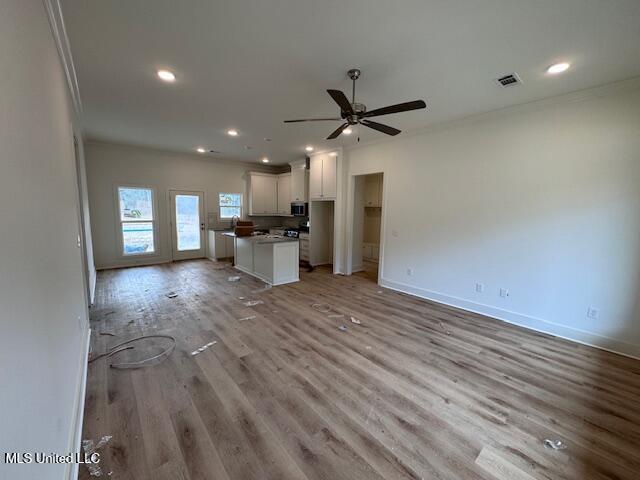 unfurnished living room with crown molding, ceiling fan, and light hardwood / wood-style flooring