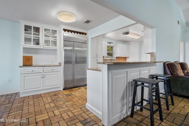 kitchen featuring white cabinetry, kitchen peninsula, dark stone counters, and built in refrigerator