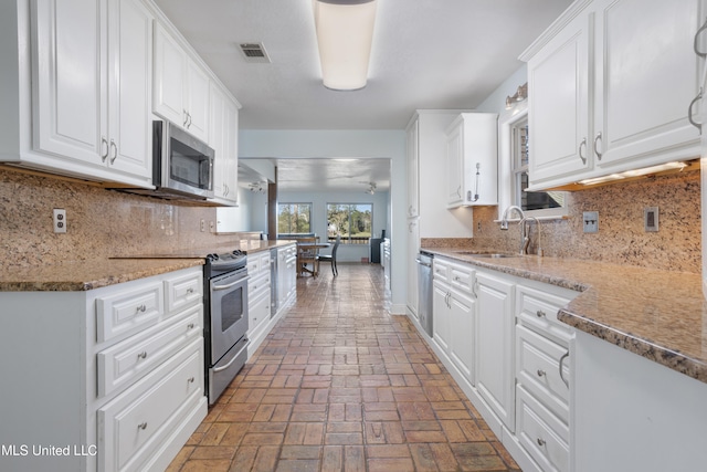 kitchen featuring white cabinetry, sink, stainless steel appliances, light stone counters, and backsplash