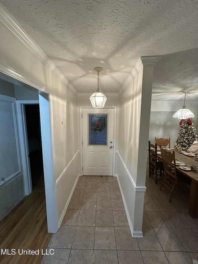 interior space with a textured ceiling, ornate columns, crown molding, and dark tile patterned flooring