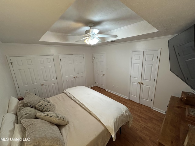 bedroom featuring ceiling fan, a raised ceiling, and multiple closets