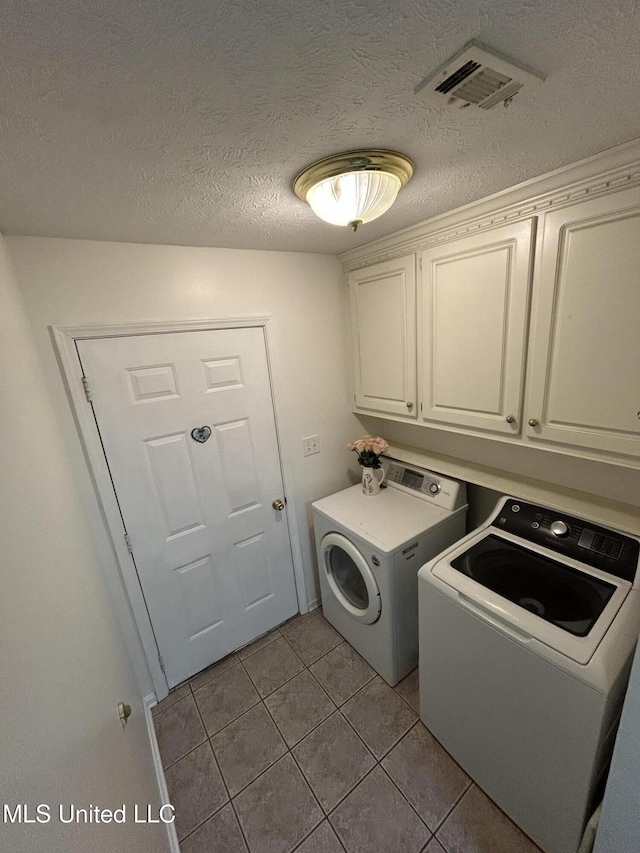 washroom featuring washer and clothes dryer, cabinets, light tile patterned floors, and a textured ceiling