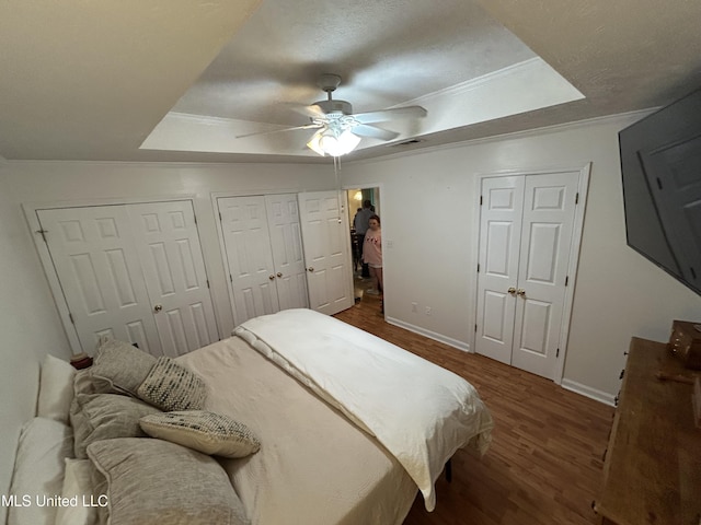 bedroom featuring ceiling fan, dark hardwood / wood-style flooring, a tray ceiling, and multiple closets