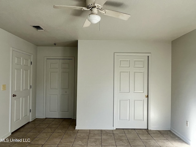 unfurnished bedroom with ceiling fan, light tile patterned flooring, and two closets