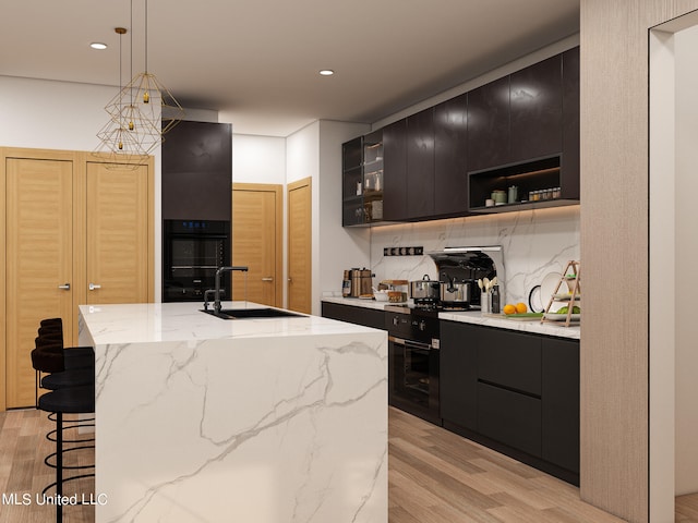 kitchen featuring decorative backsplash, hanging light fixtures, black oven, light hardwood / wood-style floors, and sink