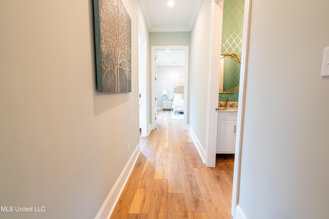 hallway with light wood finished floors, baseboards, crown molding, a sink, and recessed lighting