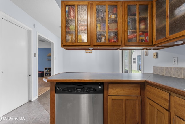 12509 Ponce De Leon Dr, Ocean Springs, MS 39564 - kitchen featuring glass insert cabinets, dishwasher, light tile patterned floors, brown cabinetry, and a peninsula