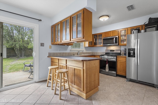 12509 Ponce De Leon Dr, Ocean Springs, MS 39564 - kitchen with a peninsula, stainless steel appliances, brown cabinetry, plenty of natural light, and visible vents