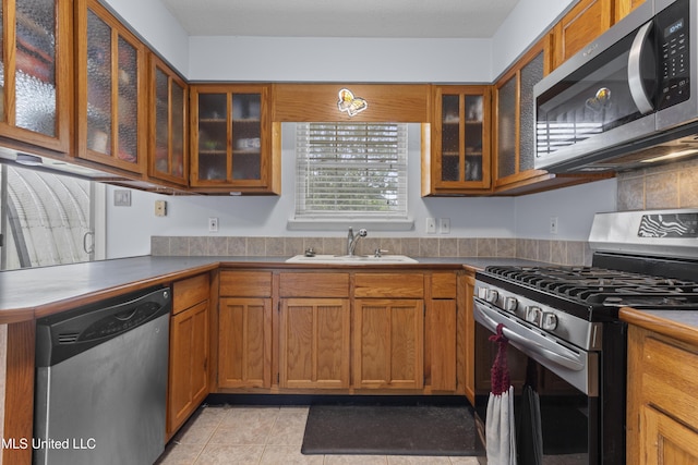 12509 Ponce De Leon Dr, Ocean Springs, MS 39564 - kitchen with a sink, brown cabinetry, light tile patterned flooring, glass insert cabinets, and appliances with stainless steel finishes
