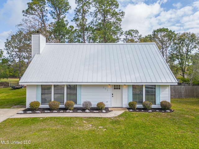 view of front facade featuring metal roof, a chimney, a front lawn, and fence