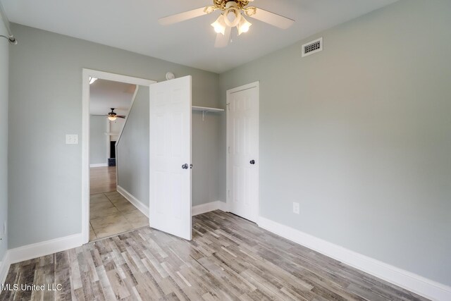 unfurnished bedroom with wood finished floors, visible vents, baseboards, ceiling fan, and a closet