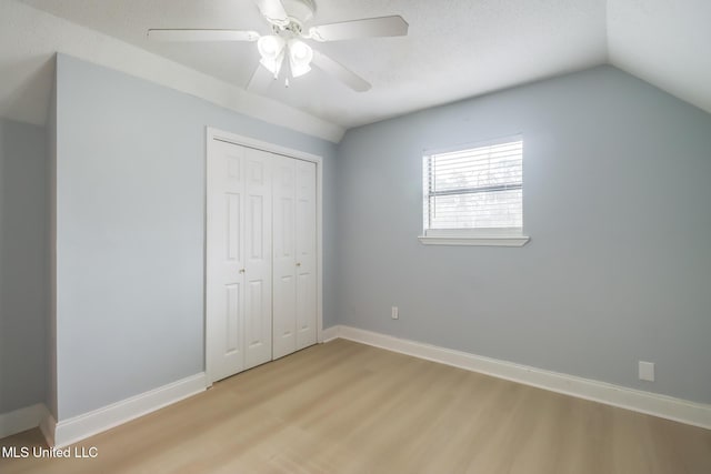 unfurnished bedroom featuring vaulted ceiling, baseboards, a closet, and light wood finished floors