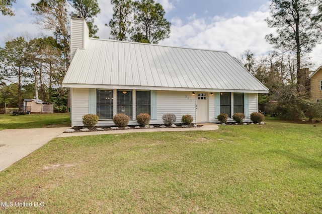 view of front of house featuring a chimney, metal roof, and a front yard