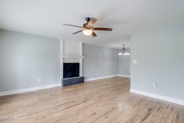 unfurnished living room featuring baseboards, light wood-style flooring, a fireplace, and ceiling fan with notable chandelier