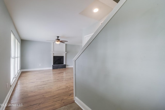 unfurnished living room featuring a fireplace, baseboards, a ceiling fan, and wood finished floors