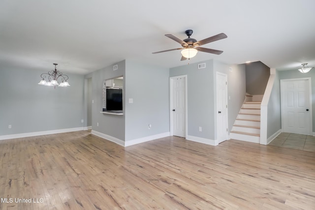 unfurnished living room with visible vents, ceiling fan with notable chandelier, light wood finished floors, baseboards, and stairs