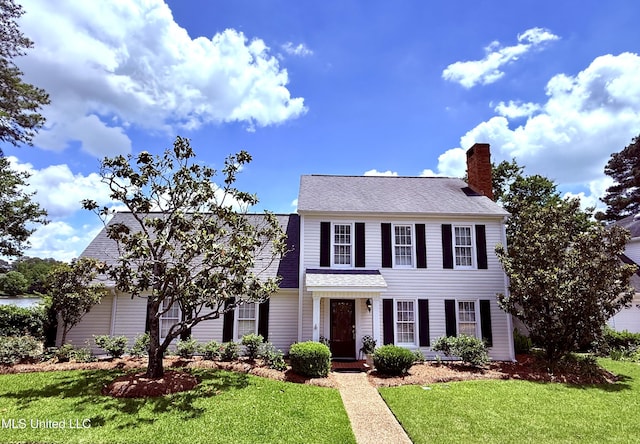 view of front of home with a front yard, a chimney, and a shingled roof