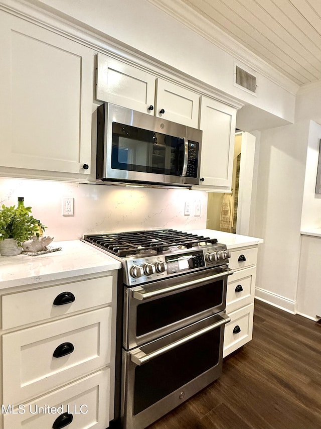 kitchen with appliances with stainless steel finishes, ornamental molding, dark wood finished floors, light countertops, and white cabinets