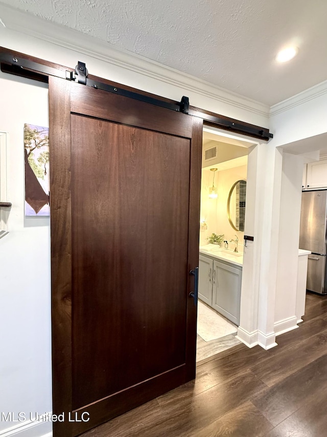 detailed view of a barn door, freestanding refrigerator, crown molding, wood finished floors, and a sink