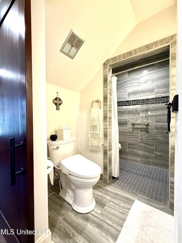 bathroom featuring lofted ceiling, toilet, tiled shower, and wood finished floors
