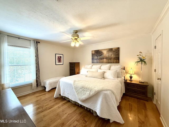 bedroom featuring wood finished floors, baseboards, crown molding, a ceiling fan, and a textured ceiling
