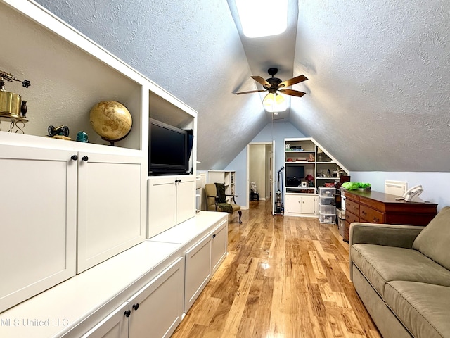 living room featuring a ceiling fan, lofted ceiling, light wood finished floors, built in shelves, and a textured ceiling