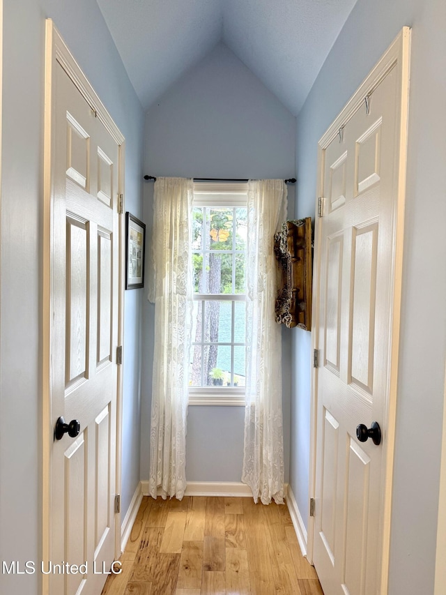 doorway to outside featuring light wood finished floors, lofted ceiling, and baseboards