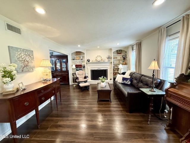 living room with dark wood-style flooring, crown molding, built in features, a fireplace with raised hearth, and recessed lighting