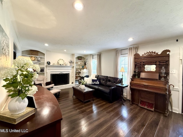 living area featuring dark wood-type flooring, ornamental molding, a fireplace, built in shelves, and a textured ceiling