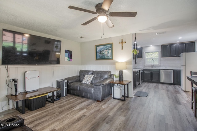 living room with a textured ceiling, ceiling fan, light wood-type flooring, and sink