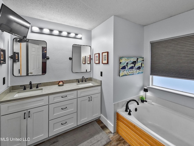 881 Brentwood Dr, Biloxi, MS 39532 - bathroom featuring wood finished floors, double vanity, a textured ceiling, and a garden tub