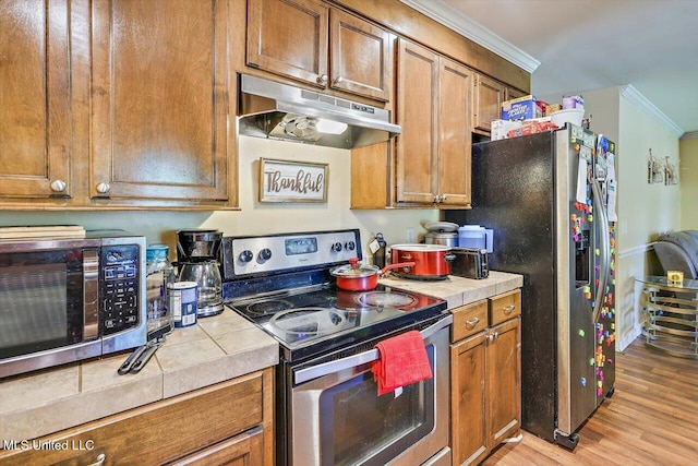 6 Laurie Cv, Byram, MS 39272 - kitchen featuring appliances with stainless steel finishes, under cabinet range hood, tile countertops, ornamental molding, and light wood-type flooring